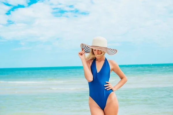 一个美丽的年轻女孩 金发在蓝色泳衣和帽子放松在阳光明媚的热天在海边的海滩 — 图库照片