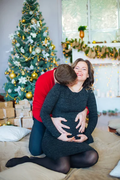 美丽的怀孕夫妇在圣诞树的背景 有一个休息的圣诞假期前的新年 大怀孕的肚子 — 图库照片