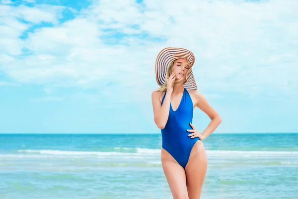 A beautiful young girl with blond hair in a blue swimsuit and hat relax on beach in the sea in sunny hot day