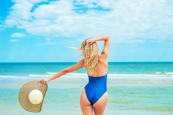 一个美丽的年轻女孩 金发在蓝色泳衣和帽子放松在阳光明媚的热天在海边的海滩 — 图库照片