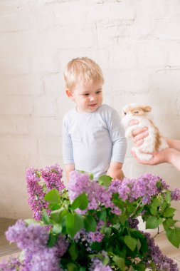 Hafif bir arka plan üzerinde bir hasır sepette leylak çiçekleri ile küçük bunnies ile sarı saçlı küçük sevimli çocuk