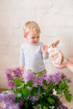 Hafif bir arka plan üzerinde bir hasır sepette leylak çiçekleri ile küçük bunnies ile sarı saçlı küçük sevimli çocuk