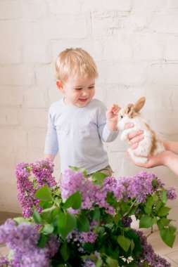 Hafif bir arka plan üzerinde bir hasır sepette leylak çiçekleri ile küçük bunnies ile sarı saçlı küçük sevimli çocuk