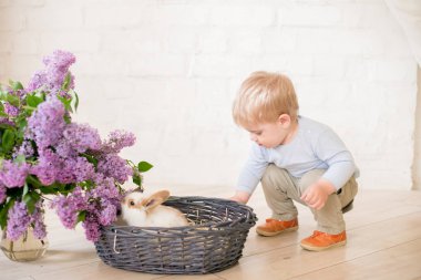 Hafif bir arka plan üzerinde bir hasır sepette leylak çiçekleri ile küçük bunnies ile sarı saçlı küçük sevimli çocuk