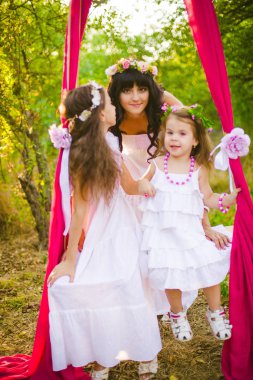 Beyaz elbiseli kızları ile genç anne salıncakta gün batımı nda bir yaz alanında eğleniyor