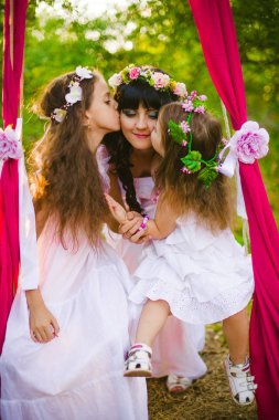 Beyaz elbiseli kızları ile genç anne salıncakta gün batımı nda bir yaz alanında eğleniyor