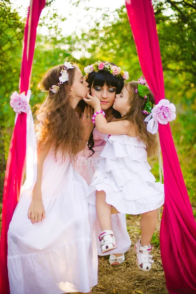 Beyaz elbiseli kızları ile genç anne salıncakta gün batımı nda bir yaz alanında eğleniyor