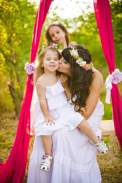 Beyaz elbiseli kızları ile genç anne salıncakta gün batımı nda bir yaz alanında eğleniyor