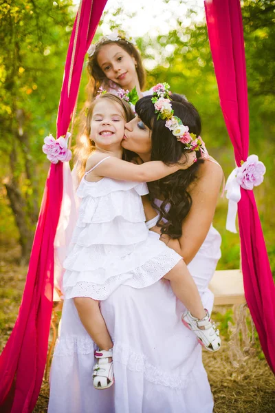 Beyaz elbiseli kızları ile genç anne salıncakta gün batımı nda bir yaz alanında eğleniyor