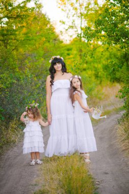 Nehir kıyısında gün batımında bir yaz tarlasında eğlenen beyaz elbiseli kızları ile genç anne