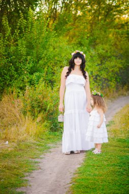 Nehir kıyısında gün batımında bir yaz tarlasında eğlenen beyaz elbiseli kızları ile genç anne