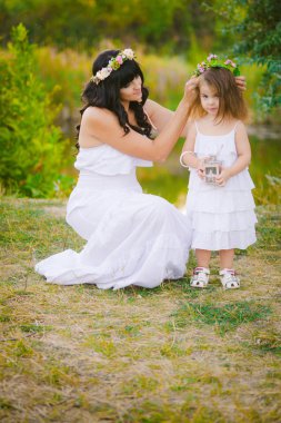 Nehir kıyısında gün batımında bir yaz tarlasında eğlenen beyaz elbiseli kızları ile genç anne