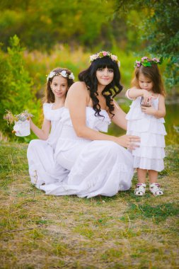 Nehir kıyısında gün batımında bir yaz tarlasında eğlenen beyaz elbiseli kızları ile genç anne