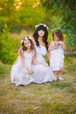 Nehir kıyısında gün batımında bir yaz tarlasında eğlenen beyaz elbiseli kızları ile genç anne