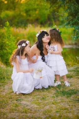 Nehir kıyısında gün batımında bir yaz tarlasında eğlenen beyaz elbiseli kızları ile genç anne