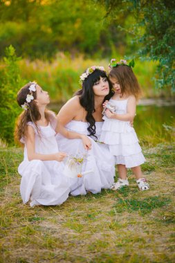 Nehir kıyısında gün batımında bir yaz tarlasında eğlenen beyaz elbiseli kızları ile genç anne