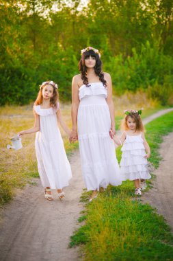 Nehir kıyısında gün batımında bir yaz tarlasında eğlenen beyaz elbiseli kızları ile genç anne