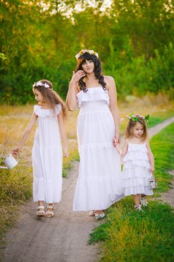 Nehir kıyısında gün batımında bir yaz tarlasında eğlenen beyaz elbiseli kızları ile genç anne