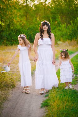 Nehir kıyısında gün batımında bir yaz tarlasında eğlenen beyaz elbiseli kızları ile genç anne