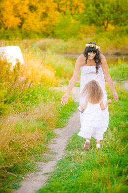 Nehir kıyısında gün batımında bir yaz tarlasında eğlenen beyaz elbiselerli kızıyla genç anne