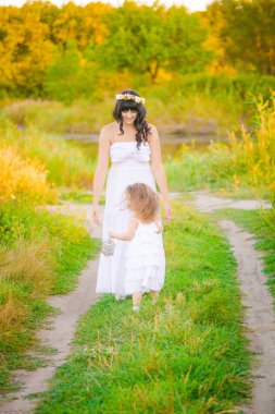 Nehir kıyısında gün batımında bir yaz tarlasında eğlenen beyaz elbiselerli kızıyla genç anne