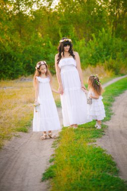 Nehir kıyısında gün batımında bir yaz tarlasında eğlenen beyaz elbiseli kızları ile genç anne