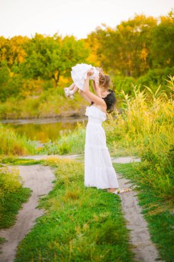 Nehir kıyısında gün batımında bir yaz tarlasında eğlenen beyaz elbiselerli kızıyla genç anne