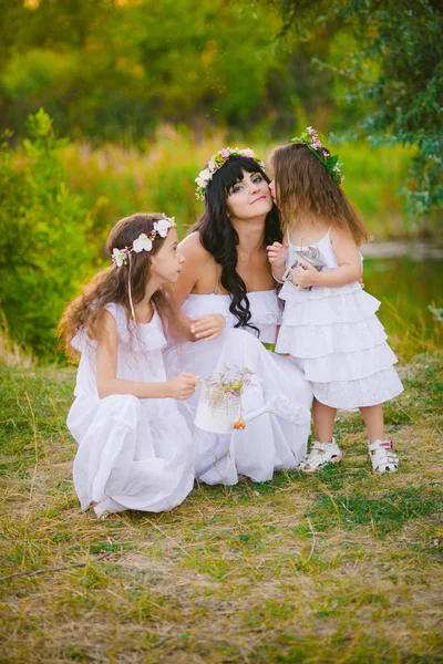 Nehir kıyısında gün batımında bir yaz tarlasında eğlenen beyaz elbiseli kızları ile genç anne