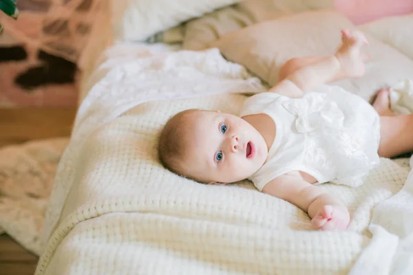 白い服を着たかわいい女の赤ちゃんがベッドの上に家に横たわり — ストック写真