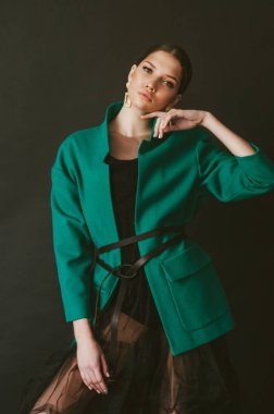 Stüdyoda siyah bir arka planda moda yeşil ceket ve mücevher koyu saçlı çekici genç kız modeli
