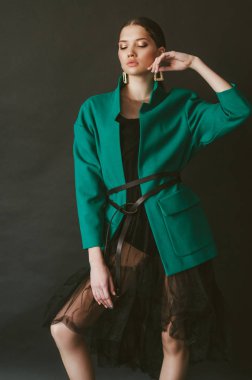 Stüdyoda siyah bir arka planda moda yeşil ceket ve mücevher koyu saçlı çekici genç kız modeli