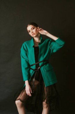 Stüdyoda siyah bir arka planda moda yeşil ceket ve mücevher koyu saçlı çekici genç kız modeli