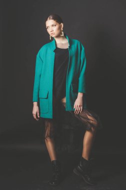 Stüdyoda siyah bir arka planda moda yeşil ceket ve mücevher koyu saçlı çekici genç kız modeli