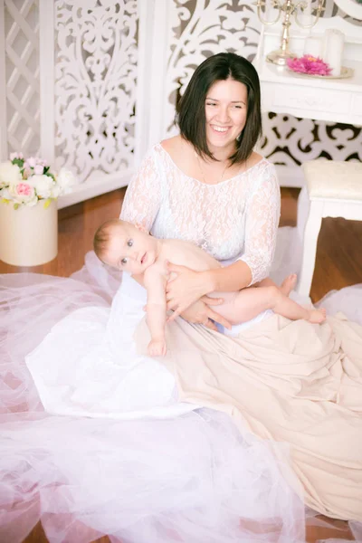 明るいブドワールの寝室で彼女の腕の中に赤ちゃんを持つ若いママ — ストック写真