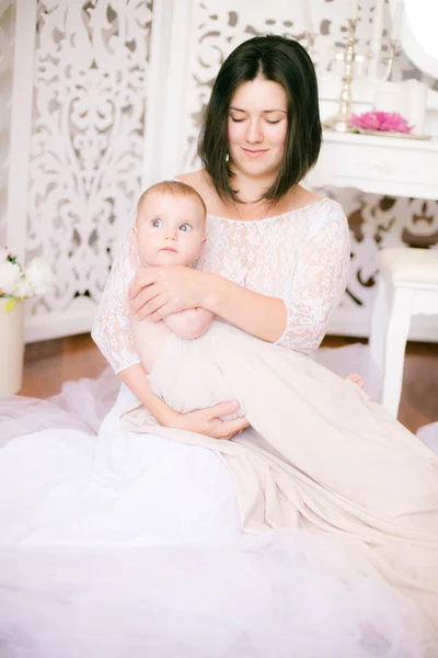 明るいブドワールの寝室で彼女の腕の中に赤ちゃんを持つ若いママ — ストック写真