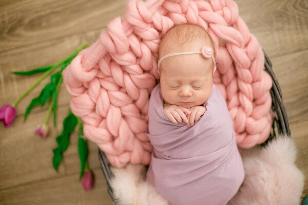 Perfect newborn baby girl in pink blanket in a wicker basket decorated with beautiful spring pink tulips