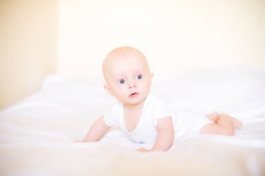 Beyaz güneşli yatak odasında beyaz giyen bebek çocuk. Yatakta rahatlatıcı yenidoğan çocuk. Çocuklar için kreş. Çocuklar için tekstil ve yatak. Evde aile sabahı. 