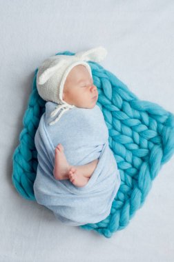 Mavi bir battaniye ve evde yatakta tavşan kulakları ile beyaz bir kap sevimli küçük bebek