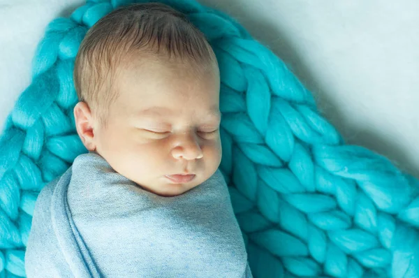 Cute little baby in a blue blanket on the bed at home