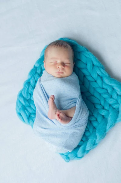 Cute little baby in a blue blanket on the bed at home