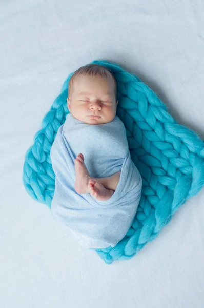 Cute little baby in a blue blanket on the bed at home