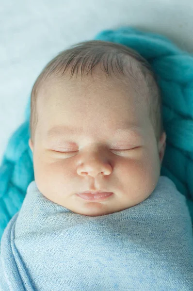 Cute little baby in a blue blanket on the bed at home