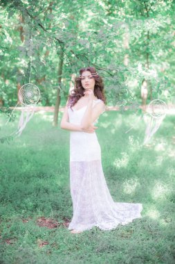 Güzel bir saç modeli ile uzun beyaz elbiseli genç çekici kız, bir yaz parkında beyaz rüya yakalayıcılar ile