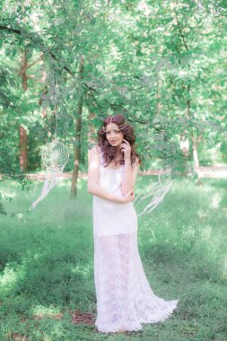 Güzel bir saç modeli ile uzun beyaz elbiseli genç çekici kız, bir yaz parkında beyaz rüya yakalayıcılar ile