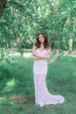 Güzel bir saç modeli ile uzun beyaz elbiseli genç çekici kız, bir yaz parkında beyaz rüya yakalayıcılar ile