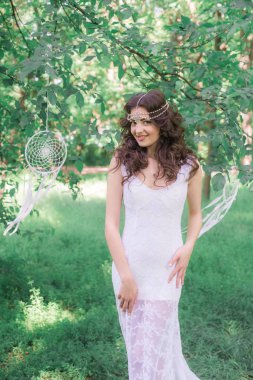 Güzel bir saç modeli ile uzun beyaz elbiseli genç çekici kız, bir yaz parkında beyaz rüya yakalayıcılar ile
