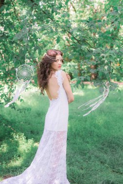 Güzel bir saç modeli ile uzun beyaz elbiseli genç çekici kız, bir yaz parkında beyaz rüya yakalayıcılar ile
