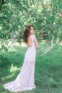 Güzel bir saç modeli ile uzun beyaz elbiseli genç çekici kız, bir yaz parkında beyaz rüya yakalayıcılar ile