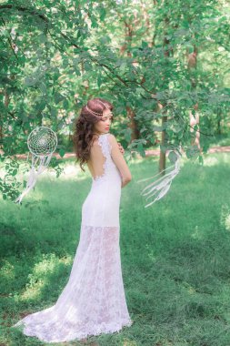 Güzel bir saç modeli ile uzun beyaz elbiseli genç çekici kız, bir yaz parkında beyaz rüya yakalayıcılar ile