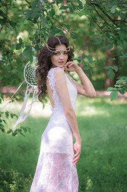 Güzel bir saç modeli ile uzun beyaz elbiseli genç çekici kız, bir yaz parkında beyaz rüya yakalayıcılar ile